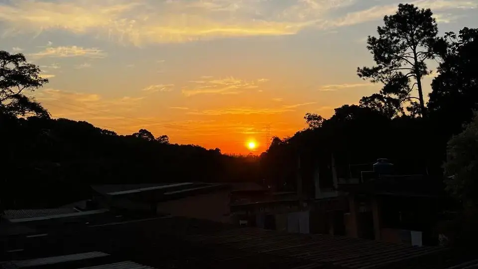 Pôr do sol visto do sítio, com o sol descendo atrás da mata